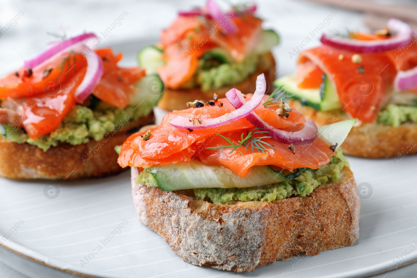 Photo of Delicious sandwiches with salmon, avocado, cucumber and onion on plate, closeup
