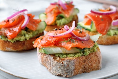 Photo of Delicious sandwiches with salmon, avocado, cucumber and onion on plate, closeup