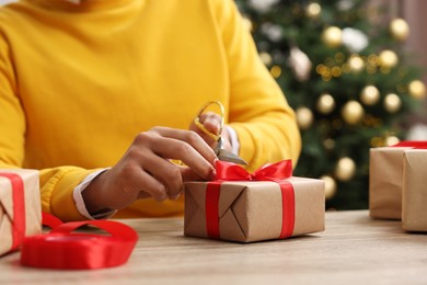 Photo of Man decorating Christmas gift box at wooden table indoors, closeup