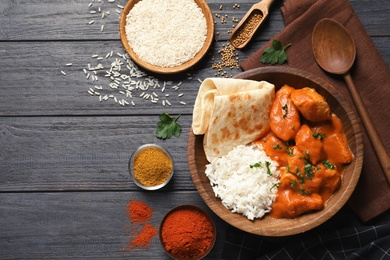 Photo of Delicious butter chicken with rice served on wooden table, flat lay. Space for text