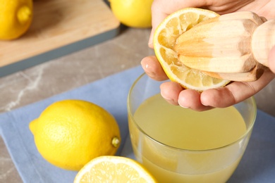 Photo of Woman squeezing lemon juice with reamer into glass on table