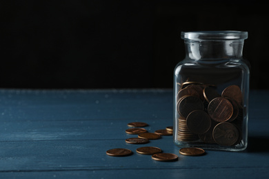 Photo of Glass jar with coins on blue wooden table, space for text