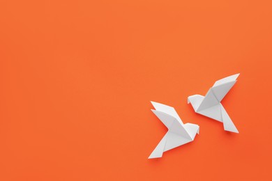 Photo of Beautiful white origami birds on orange background, flat lay. Space for text