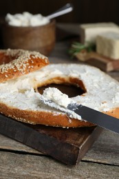 Photo of Delicious bagel with tofu cream cheese and knife on wooden table, closeup