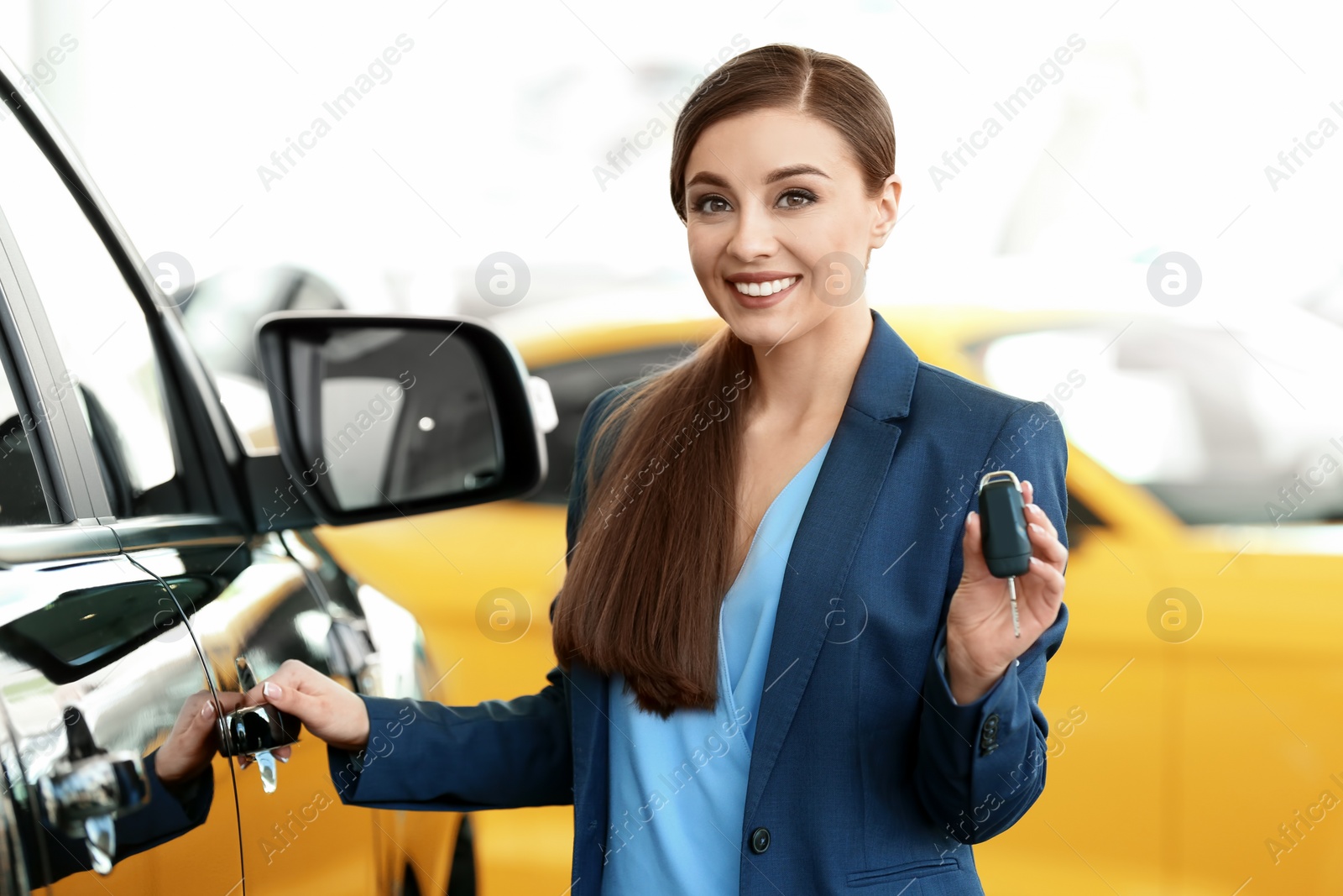 Photo of Young woman holding key near new car in salon