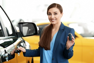 Young woman holding key near new car in salon