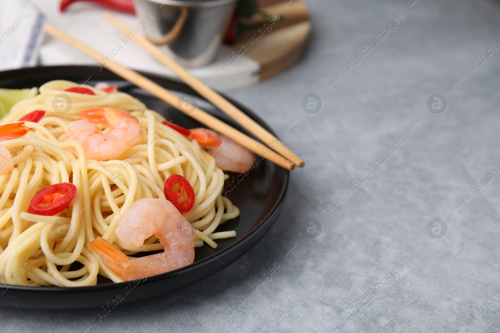 Photo of Tasty spaghetti with shrimps and chili pepper on grey table, closeup. Space for text