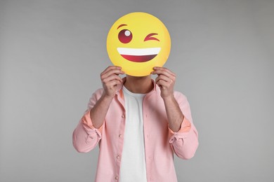 Man covering face with happy winking emoticon on grey background