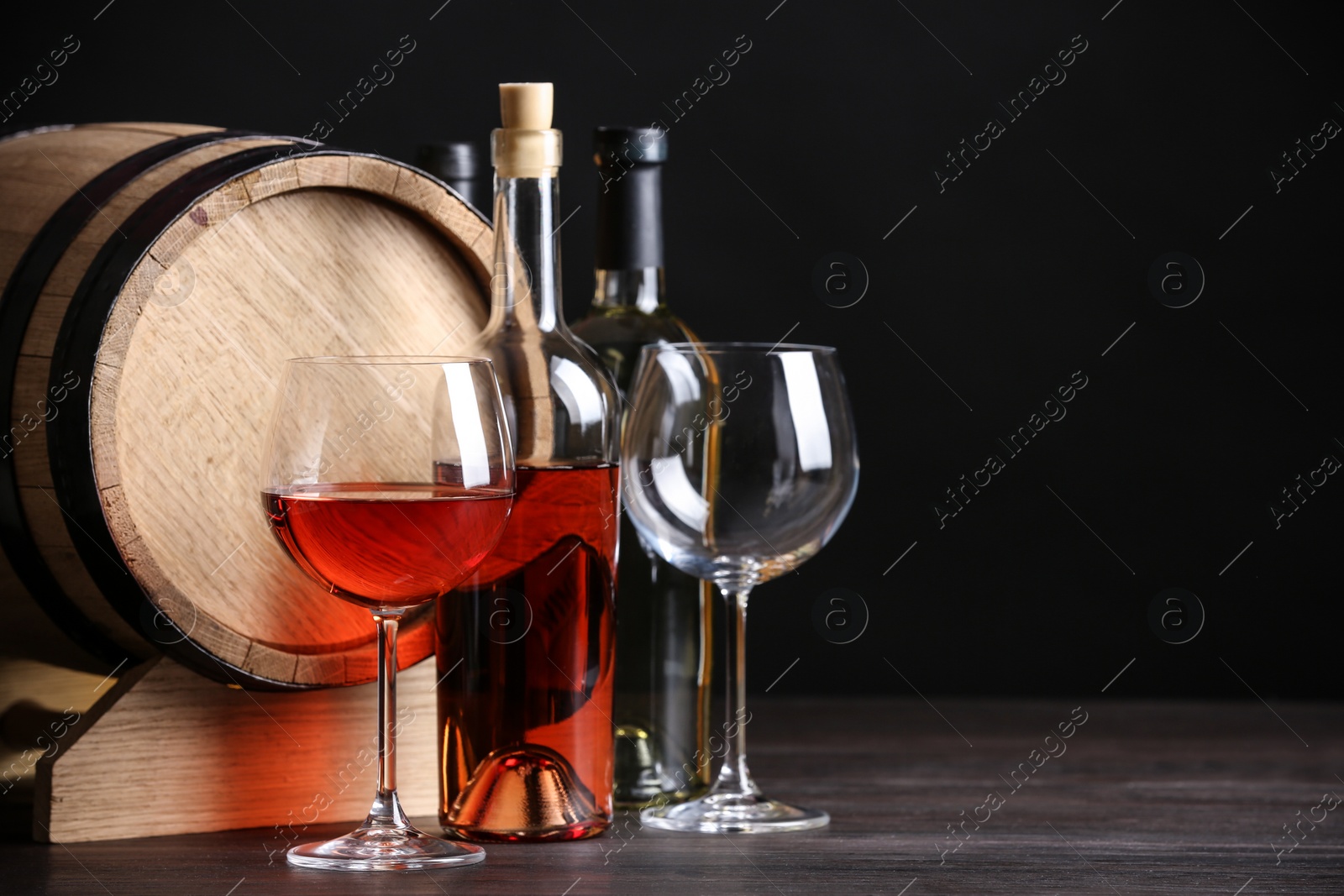 Photo of Wooden cask, glasses and bottles of wine on table against dark background, space for text