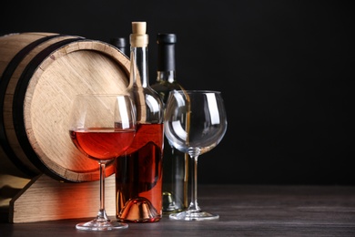 Photo of Wooden cask, glasses and bottles of wine on table against dark background, space for text