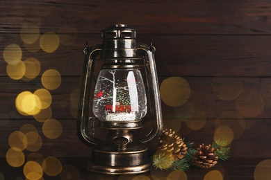 Image of Beautiful Christmas snow globe in vintage lantern on wooden background, bokeh effect