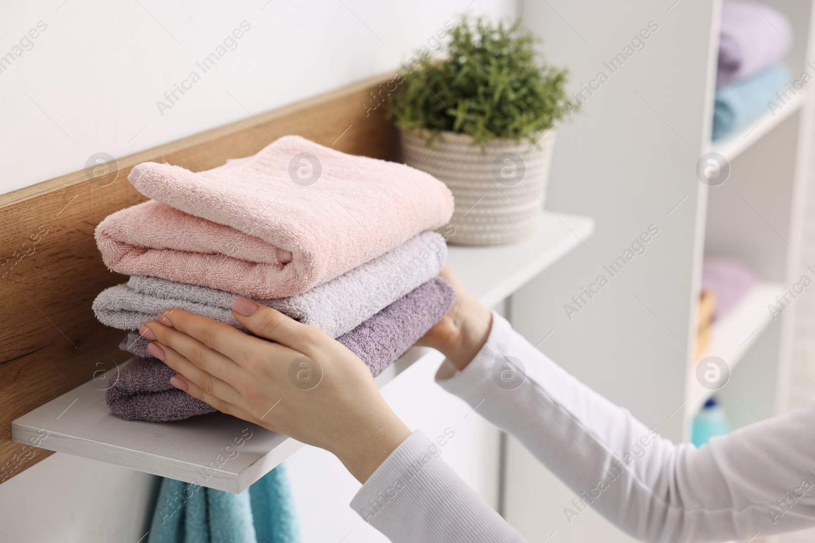 Photo of Woman stacking clean towels on shelf indoors, closeup