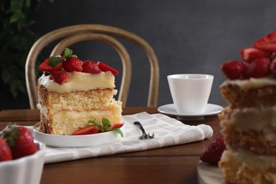 Photo of Piece of tasty cake with fresh strawberries, mint and cup of tea on wooden table