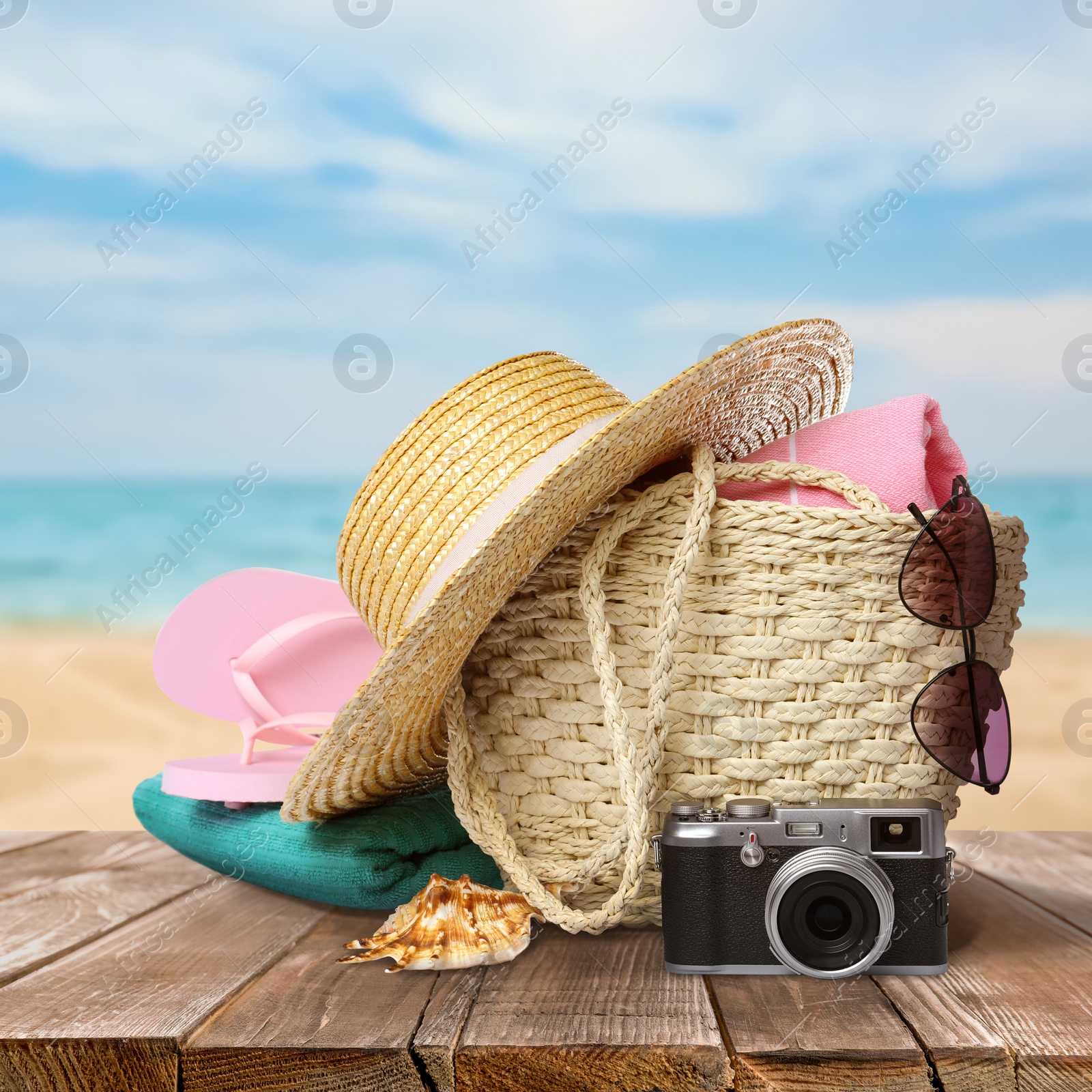 Image of Stylish bag with beach accessories on wooden surface near seashore 