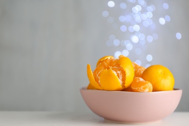 Photo of Tangerines in bowl on table against blurred lights, space for text
