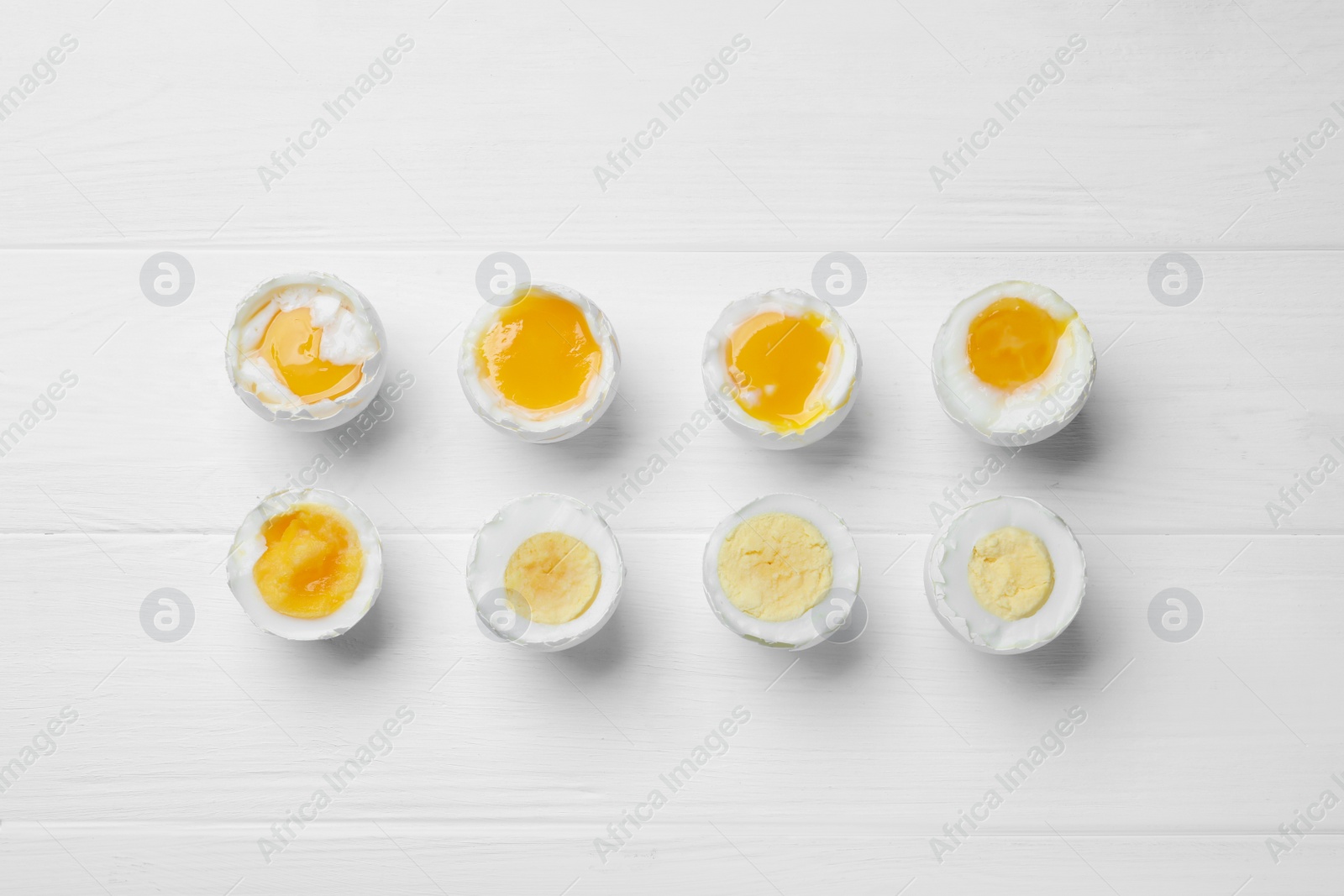 Photo of Different readiness stages of boiled chicken eggs on white wooden table, flat lay