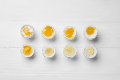 Photo of Different readiness stages of boiled chicken eggs on white wooden table, flat lay