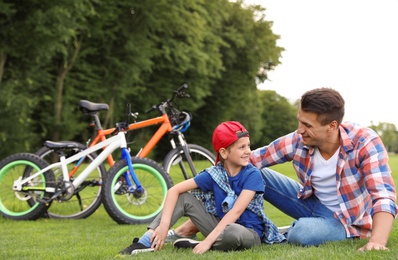 Dad and son sitting near their bicycles outdoors