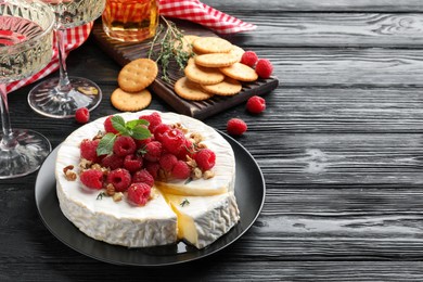 Photo of Brie cheese served with raspberries and walnuts on black wooden table. Space for text