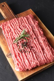 Photo of Raw ground meat, rosemary and peppercorns on black table, above view