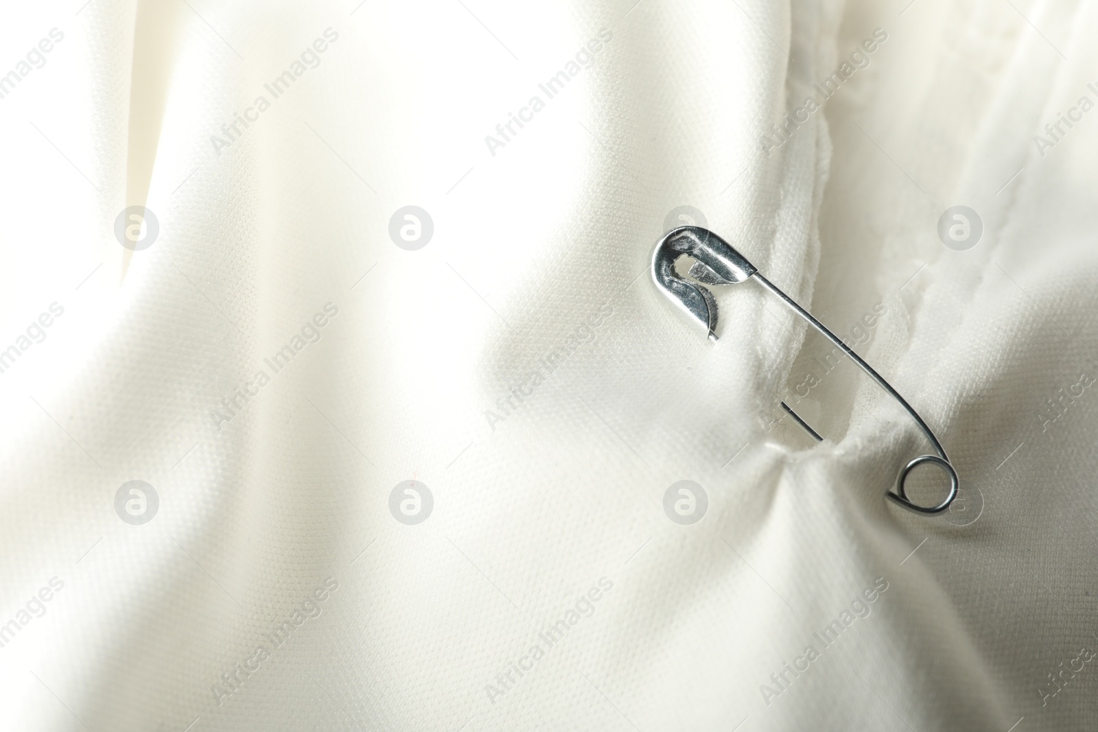 Photo of Metal safety pin on white fabric, closeup