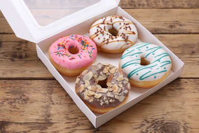 Photo of Box with different tasty glazed donuts on wooden table