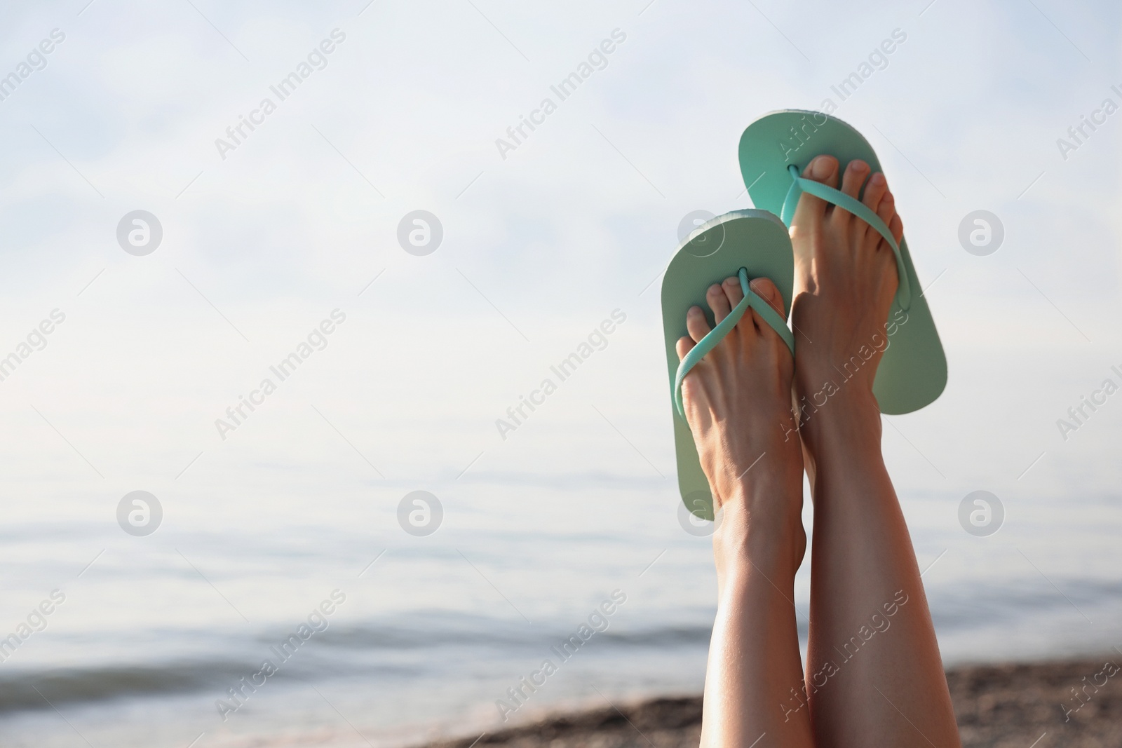 Photo of Woman in stylish flip flops near sea, closeup. Space for text