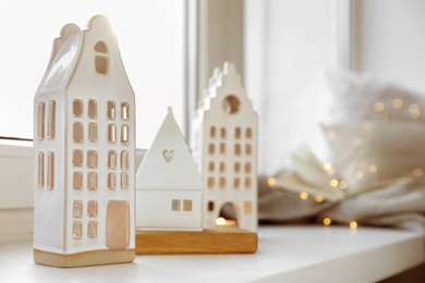 Photo of Beautiful house shaped candle holders and festive lights on windowsill indoors, space for text