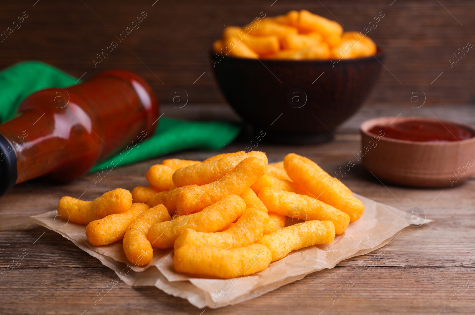 Photo of Crunchy cheesy corn snack and ketchup on wooden table, closeup