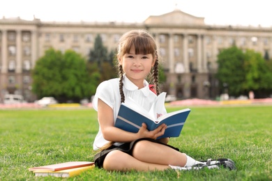 Photo of Schoolgirl with stationery sitting on grass outdoors