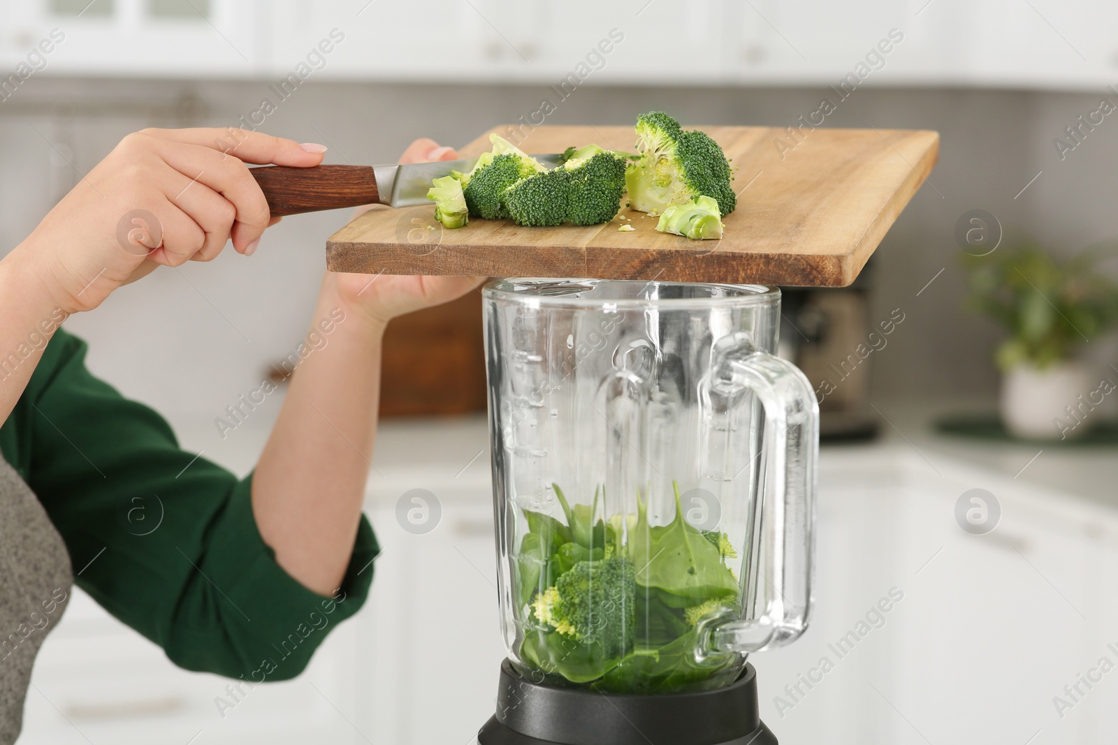 Photo of Woman adding broccoli into blender with ingredients for smoothie in kitchen, closeup
