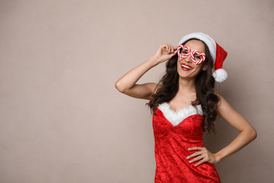 Beautiful woman in Christmas costume with party glasses on beige background, space for text