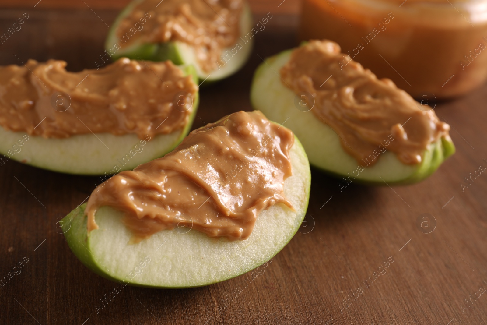 Photo of Slices of fresh apple with nut butter on wooden board, closeup