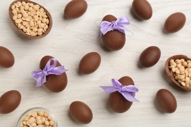 Photo of Sweet chocolate eggs with bows and candies on white wooden table, flat lay