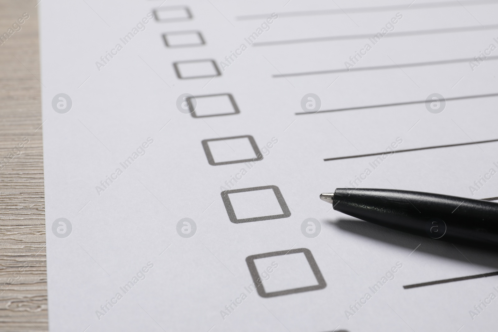 Photo of Paper sheet with checkboxes and pen on wooden table, closeup. Checklist