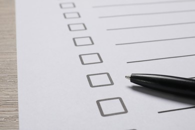 Photo of Paper sheet with checkboxes and pen on wooden table, closeup. Checklist