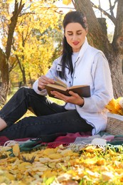 Photo of Happy woman reading book in park on autumn day