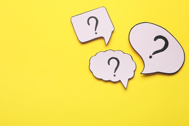 Photo of Paper speech bubbles with question marks on yellow background, flat lay. Space for text