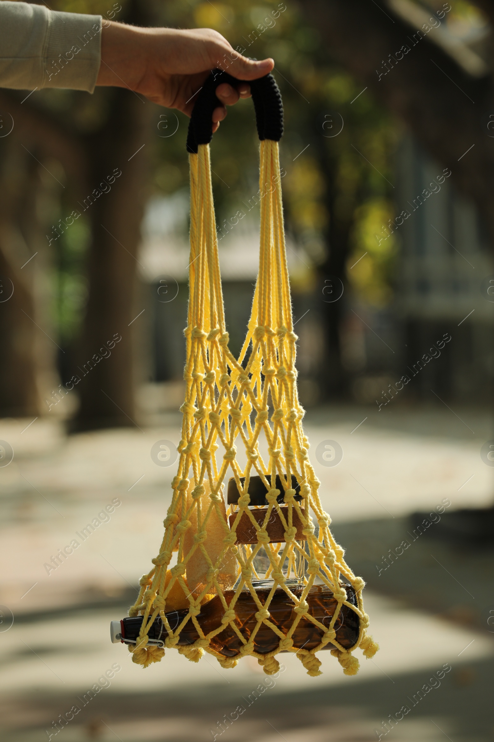 Photo of Conscious consumption. Woman with net bag of eco friendly products outdoors, closeup