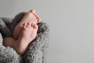 Photo of Little baby with cute feet wrapped in soft blanket against grey background, closeup. Space for text