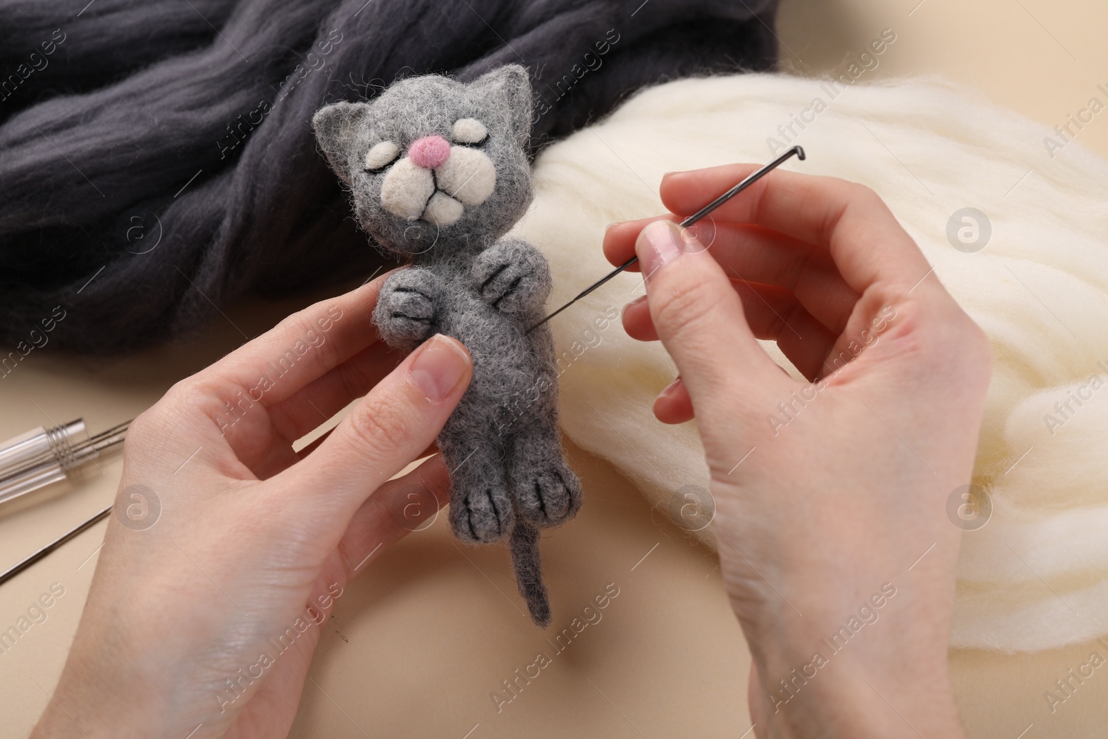 Photo of Woman felting cute toy cat from wool at beige table, closeup