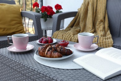 Outdoor breakfast with tea, croissants and book on rattan table on terrace