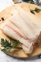 Pieces of raw cod fish, spices and parsley on table