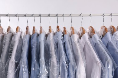 Photo of Hangers with shirts in dry cleaning plastic bags on rack against light background