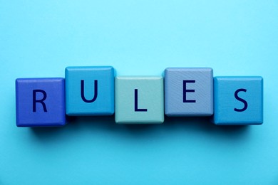 Word Rules made of wooden cubes with letters on light blue background, flat lay