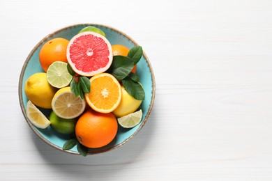 Photo of Different cut and whole citrus fruits on white wooden table, top view. Space for text