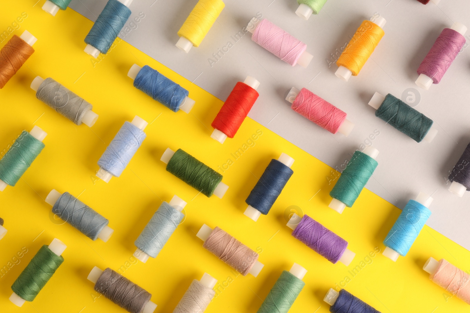 Photo of Different sewing threads on color background, flat lay