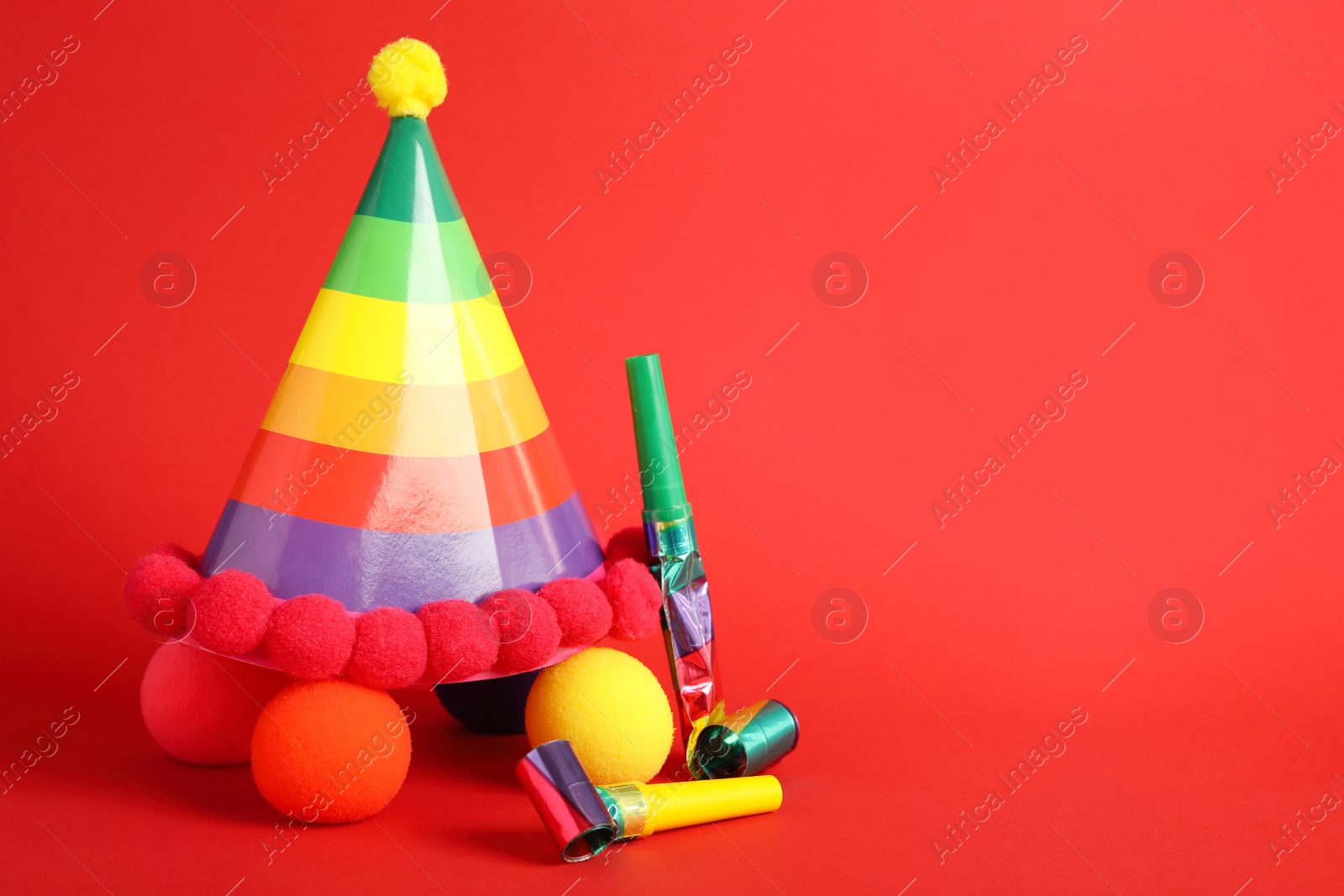 Photo of Party cap, blowers and clown noses on red background, space for text