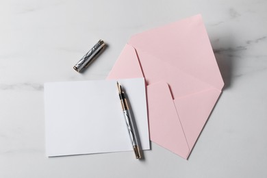 Photo of Blank sheet of paper, pen and letter envelope on white marble table, top view. Space for text