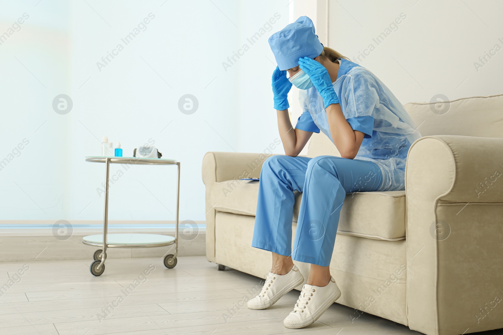 Photo of Exhausted doctor sitting on sofa indoors. Stress of health care workers during COVID-19 pandemic